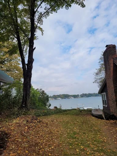 Lake view through trees with brick house and fallen autumn leaves